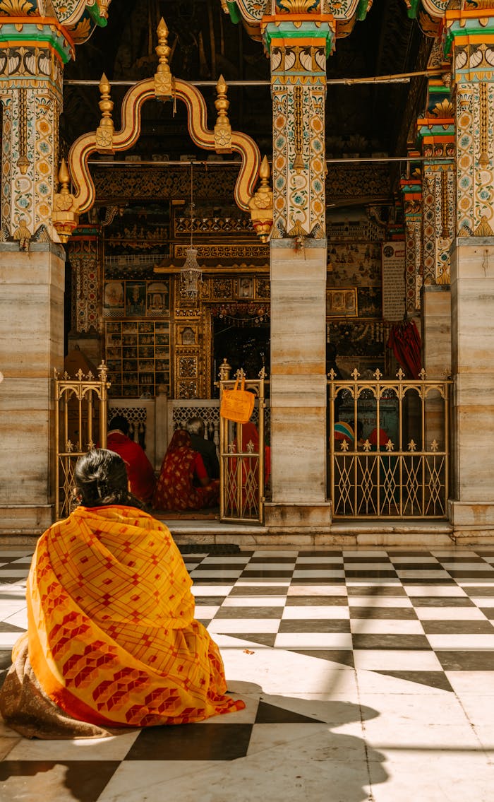 A woman in vibrant sari prays outside an ornate Indian temple, capturing spirituality and tradition.