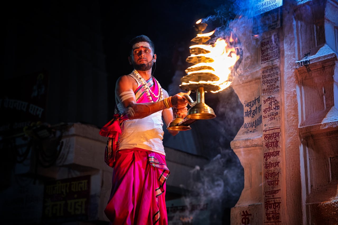 Hindu priest in Deoghar, India performing ritual with fire at night, showcasing traditional attire and ceremonial practice.